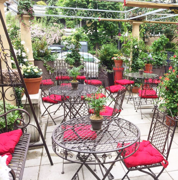 Gemütlicher Gartenbereich von Denny's Café & Wein mit schmiedeeisernen Tischen